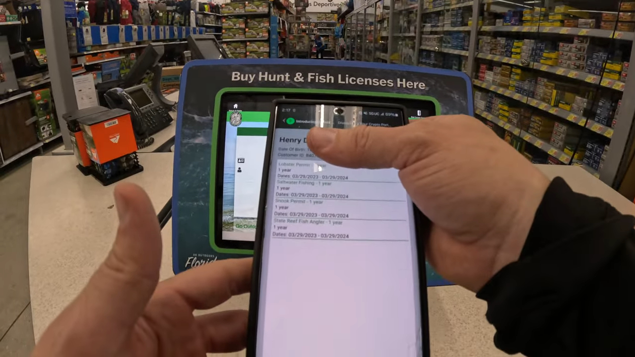 Person using a mobile phone to check fishing license details near a kiosk in Walmart