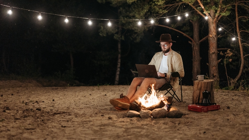 Man working on a laptop by a campfire at night, showing remote engagement and loyalty-building for an putdoor brand