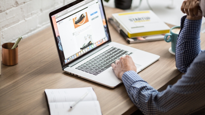 Person browsing outdoor gear on a laptop while taking notes