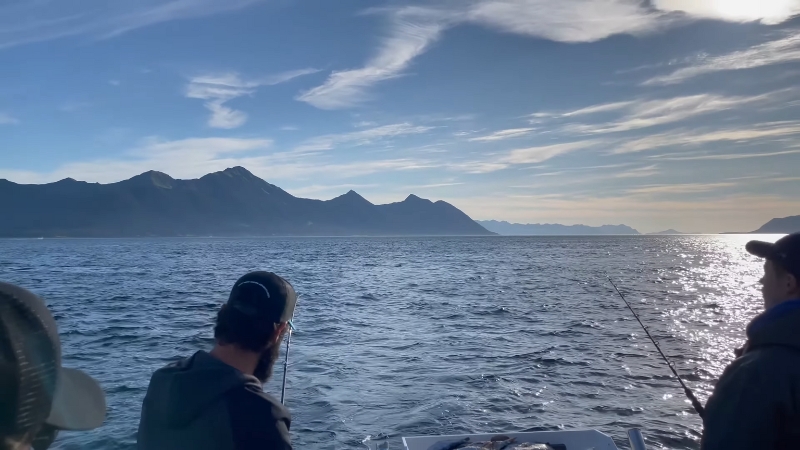 Friends fish together on open water with mountains in the background