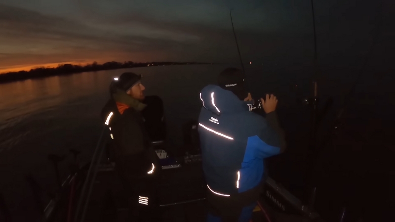 Two anglers stand on a boat at dusk preparing rods for night fishing on Lake Erie