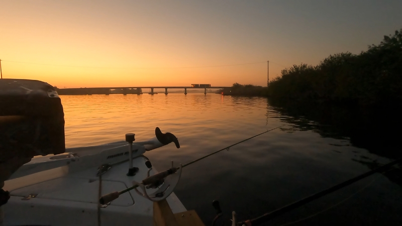 A boat sits near the shoreline on Lake Okeechobee at dusk with fishing rods set up over calm water
