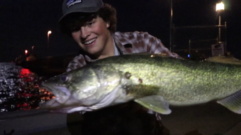 A smiling angler holds a walleye at night on Lake St. Clair near dock lights