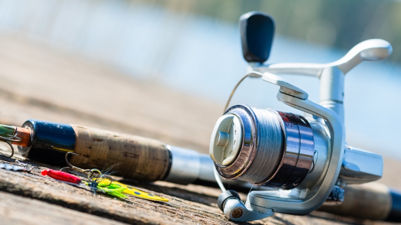 A spinning rod and reel rest on a wooden dock beside a few small lures