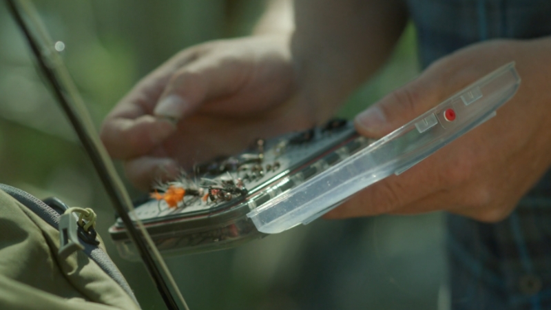 An angler selects fly lures from a small case during a trip