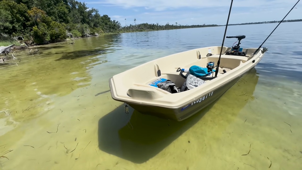 A small jon boat rests in clear shallow lake water near a wooded shoreline
