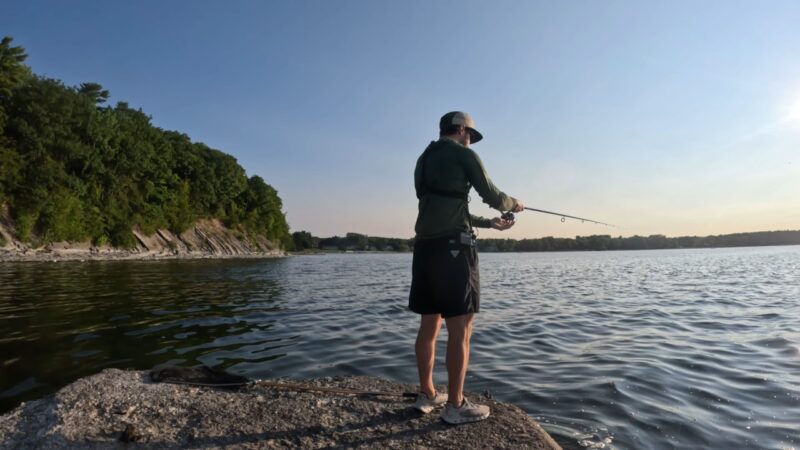 Angler casts on a rocky Lake Champlain shore at sunset