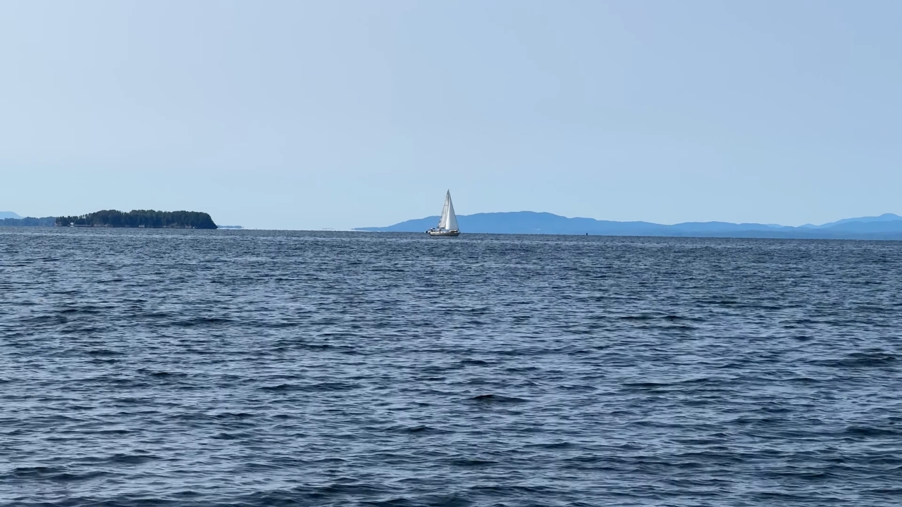 A sailboat crosses Lake Champlain with blue mountains in the distance