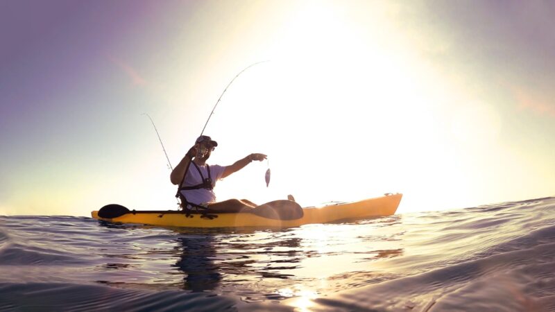A man in a yellow kayak holds a fish on open water at sunset